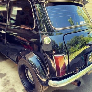 A close-up of a black classic mini cooper featuring a personalized black leather gas tank bib, showcasing a stylish and sophisticated automotive accessory