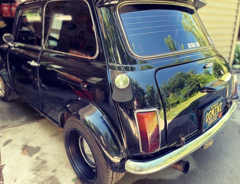 A close-up of a black classic mini cooper featuring a personalized black leather gas tank bib, showcasing a stylish and sophisticated automotive accessory