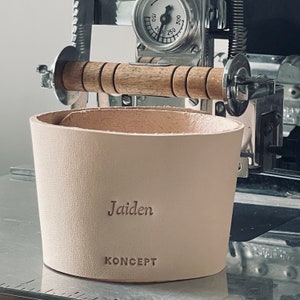 A personalized coffee cozy with the name "Jaiden" on it, placed on a machine. Handmade from Italian leather for ultimate comfort