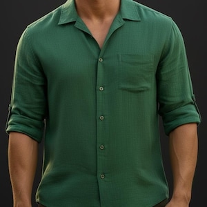 May include: A long-sleeved button-down shirt in a solid forest green color. The shirt features a classic collar, a single chest pocket on the left side, and sleeves that are rolled up to the elbows with buttoned tabs to secure the cuffs in place.