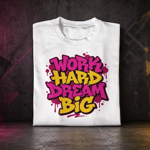 Peut inclure: Un t-shirt blanc arborant un motif graphique central avec le texte "WORK HARD DREAM BIG" écrit dans une police de style graffiti. Les mots "WORK" et "DREAM" sont en rose vif, tandis que "HARD" et "BIG" sont d'une couleur jaune audacieuse.