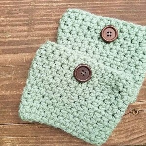 May include: Two crocheted wrist warmers in a light green color with brown buttons.