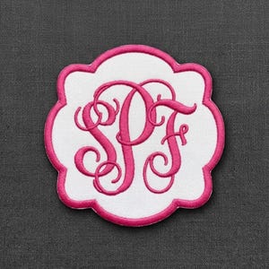 May include: A white, scalloped-edge patch featuring a hot pink embroidered monogram with the letters SPF in a decorative, swirling script font. The patch has a thick, hot pink stitched border that follows the shape of the scalloped edges.