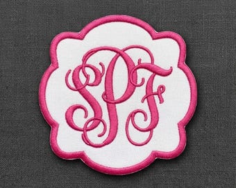 Può includere: Una toppa bianca con bordi smerlati caratterizzata da un monogramma ricamato in rosa acceso con le lettere SPF in un carattere corsivo decorativo e sinuoso. La toppa presenta un bordo spesso cucito in rosa acceso che segue la forma smerlata.