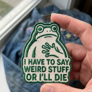 May include: An embroidered patch featuring a white frog with green outlines and details. The frog has one hand placed on its chest. Below the frog, the text reads: I HAVE TO SAY WEIRD STUFF OR I'LL DIE in bold, green, capital letters.