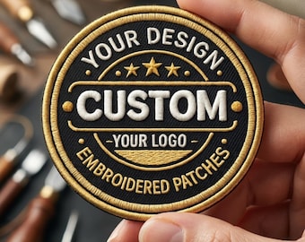 May include: A circular embroidered patch featuring a black background with gold and white stitching. The text reads YOUR DESIGN, CUSTOM, YOUR LOGO, and EMBROIDERED PATCHES, with three gold stars centered above the word CUSTOM in a white rectangular frame.