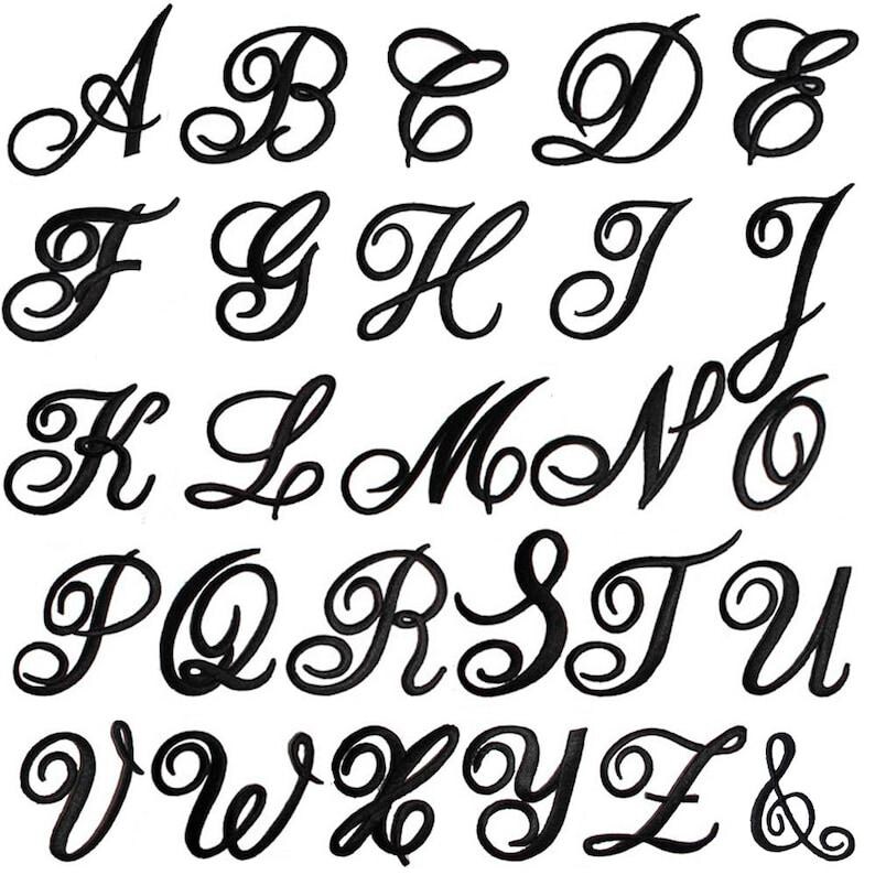 K&ouml;nnte beinhalten: Eine Sammlung von schwarzen gestickten Buchstaben des Alphabets von A bis Z sowie ein Et-Zeichen. Jeder Buchstabe weist einen dekorativen, flie&szlig;enden Schreibschriftstil mit kr&auml;ftigen Linien und kunstvollen, eleganten Schleifen auf.