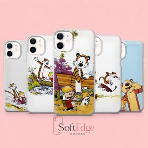 May include: Five clear phone cases featuring various illustrations of a boy and a tiger character. The designs include the characters in a red wagon, crossing a log over a stream, holding a globe, and making faces. The text SoftEdge COVERS is visible.