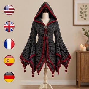 May include: A dark gray crochet hooded cardigan featuring long flared sleeves and a deep red trim along the edges. The garment includes a circular metal clasp at the neckline with a tree design and two dangling decorative accents.