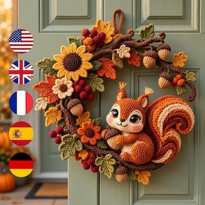 May include: A crochet wreath featuring a central orange squirrel holding an acorn, surrounded by autumn-themed elements including yellow sunflowers, orange and green maple leaves, small red berries, and brown acorns attached to a dark brown branch base.