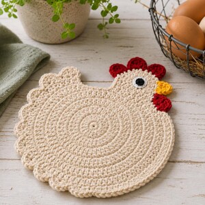 May include: A beige crochet trivet shaped like a chicken with a circular body, a scalloped edge, and a head featuring a red comb, a yellow beak, and a black and white eye. The crochet work is constructed in a spiral pattern using light yarn.
