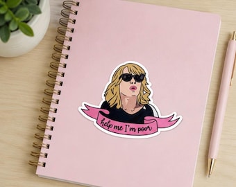May include: A die-cut sticker featuring a blonde person with sunglasses and a black shirt, positioned above a pink banner with the black text "help me I'm poor". The sticker is placed on a light pink spiral-bound notebook with a matching pink pen.