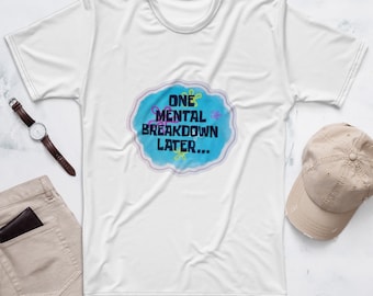 May include: A white short-sleeved t-shirt featuring a central blue cloud-shaped graphic with the text "ONE MENTAL BREAKDOWN LATER..." in dark blue letters, accented by small yellow and pink flower outlines, accompanied by a watch, cap, and pants.