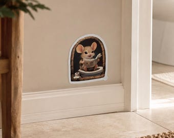 May include: A wall decal featuring a light brown mouse with large ears sitting on a toilet inside a dark arched frame, holding a newspaper. The mouse has a small smile and is positioned within a white border, creating a whimsical scene.