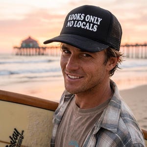 May include: A black trucker hat featuring a mesh back and a solid front panel with the white text "KOOKS ONLY NO LOCALS" printed in a bold, sans-serif font. The hat has a curved brim and a structured crown design.