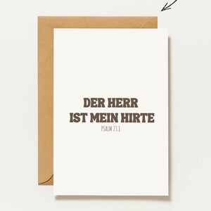 Puede incluir: Una tarjeta de felicitación blanca con un sobre marrón que presenta el texto en alemán 'DER HERR IST MEIN HIRTE' y 'PSALM 23.1' en una fuente negrita de color marrón oscuro. Sobre la tarjeta, la palabra 'PERSONALISIERBAR' con una flecha.