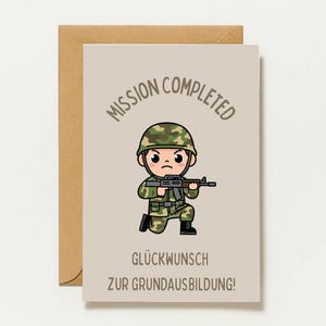 May include: A greeting card with a light beige background featuring a cartoon soldier in camouflage uniform holding a rifle. The text reads MISSION COMPLETED, GLÜCKWUNSCH ZUR GRUNDAUSBILDUNG!, and designed by Stud. A brown envelope is positioned behind the card.