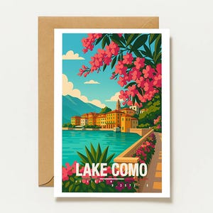 May include: A rectangular greeting card featuring a colorful illustration of Lake Como with pink flowers in the foreground, a blue lake, and orange buildings. The text LAKE COMO is printed in white, along with coordinates. A brown envelope is behind the card.