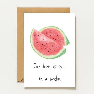 Könnte beinhalten: Eine weiße Grußkarte mit einer Aquarellillustration einer aufgeschnittenen Wassermelone mit rosa Fruchtfleisch und schwarzen Kernen. Unter der Frucht steht der Text: Our love is one in a melon. Die Karte wird mit einem braunen Umschlag geliefert.