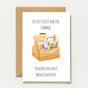 Puede incluir: Una tarjeta de felicitación blanca con sobre marrón que presenta una ilustración en acuarela de una caja de herramientas de madera llena de utensilios y una pancarta que dice HAPPY BIRTHDAY. El texto superior dice DU BIST NICHT NUR DER HAMMER, y el inferior SONDERN DER GANZE WERKZEUGKASTEN!