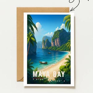 May include: A rectangular greeting card featuring a vibrant illustration of Maya Bay with turquoise water, a sandy beach, palm trees, and limestone cliffs. The text reads MAYA BAY with coordinates below. A brown envelope is positioned behind the card.