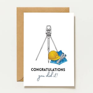 May include: A white greeting card featuring a black line drawing of a surveying total station on a tripod, a yellow hard hat, and blue rolled blueprints. The text reads CONGRATULATIONS you did it! The card is placed against a brown envelope.