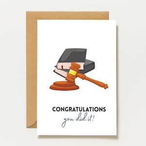 Könnte beinhalten: Eine weiße Grußkarte mit braunem Umschlag, die einen braunen Holzhammer und zwei schwarze Gesetzbücher zeigt. Der Text auf der Karte lautet CONGRATULATIONS you did it! Am unteren Rand der Karte steht der Text designed by Napel Studio.