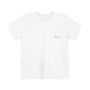 May include: A plain white short-sleeved t-shirt featuring a single chest pocket on the left side. The pocket is embroidered with the dark red capital letters NA in a serif font. The shirt has a crew neckline and a standard straight hemline.