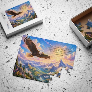 Puede incluir: Un rompecabezas con un águila calva sobrevolando un paisaje montañoso al atardecer. El texto dice: But those who hope in the Lord will renew their strength. They will soar on wings like eagles. Isaiah 40:31. Incluye una caja de color blanco.