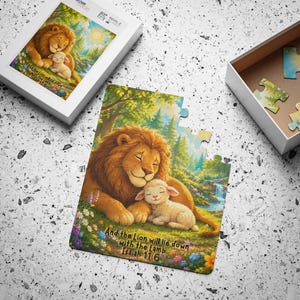 Op de afbeelding: Een legpuzzel met een gouden leeuw en een wit lammetje die samen rusten in een kleurrijke weide met bomen en een waterval. De tekst "And the Lion will lie down with the Lamb Isaiah 11:6" staat onderaan de afbeelding op de puzzel gedrukt.