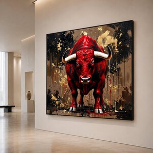 May include: A large rectangular wall art piece featuring a vibrant red bull with prominent white horns. The bull is centred against a dark, textured background with abstract splashes of metallic gold paint and black drips, framed in a thin black border.