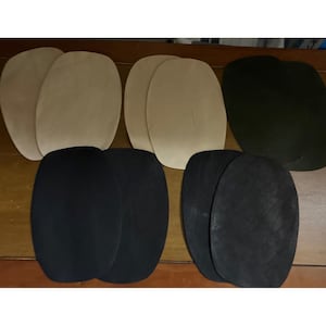 May include: A collection of ten oval-shaped leather patches arranged in two rows. The set includes four light beige patches, two dark olive green patches, and four black patches. Each patch features a smooth, matte surface and rounded edges.