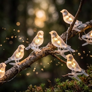May include: A string of decorative bird-shaped lights featuring translucent, clear plastic bodies that glow with a warm yellow illumination. Each bird figure is attached to a small, clear plastic clip designed to secure the light onto a branch.