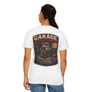 May include: A white short-sleeve t-shirt featuring a large graphic on the back. The graphic depicts a car engine in a workshop with the text GARAGE Print Studio, BUILT FOR SPEED, BUILT TO LAST, HORSEPOWER BUILT LEGENDS LAST, and BUILT NOT BOUGHT.