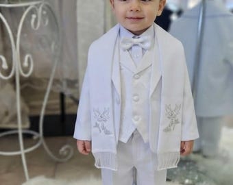 Puede incluir: Un traje formal blanco que consta de pantalones, camisa abotonada, chaleco con un patrón sutil, pajarita a juego y americana. Una estola blanca con motivos bordados en plata de cruces y palomas y flecos cuelga sobre los hombros.