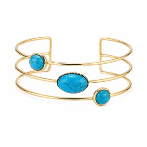 Pode incluir: Uma pulseira tipo bracelete em tom dourado com três bandas finas e paralelas. O design apresenta três pedras de cor turquesa com veios escuros: uma pedra oval grande no centro e duas pedras redondas menores nas bandas exteriores.
