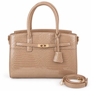 Könnte beinhalten: Eine taupefarbene Handtasche mit glänzender Krokodilprägung, ausgestattet mit zwei Tragegriffen, einem goldfarbenen Metallverschluss an einem horizontalen Riemen und einem abnehmbaren, passenden Schulterriemen, der seitlich aufgerollt ist.