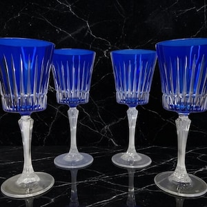 May include: A set of four cobalt blue crystal wine glasses featuring vertical cut patterns on the bowls and clear, faceted stems. Each glass has a wide, circular base and a flared rim, showcasing a deep blue color contrasted with clear glass.