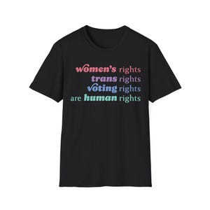 May include: A black short-sleeved t-shirt featuring the text "Women's rights trans rights voting rights are human rights" printed in four distinct colors: pink, purple, blue, and light green, arranged in four stacked lines on the front.
