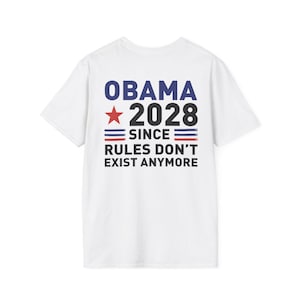 以下が含まれることがあります： 背面にグラフィックプリントが施された白い半袖Tシャツ。テキストには「OBAMA 2028」と赤い星、そして「SINCE RULES DON'T EXIST ANYMORE」というフレーズが記されており、赤と青の水平ストライプがデザインされています。