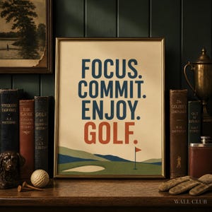 May include: A framed wall art print featuring the text FOCUS. COMMIT. ENJOY. GOLF. in blue and orange lettering. The design includes a stylized illustration of a green golf course with a sand bunker and a red flag on a pole at the bottom.