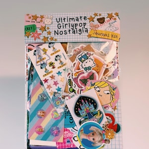 May include: A journal kit in a clear plastic bag with a header card reading Ultimate Girlypop Nostalgia Journal Kit. The kit contains various stickers, including cartoon characters, a castle, and stars, along with a metal paperclip and charms.