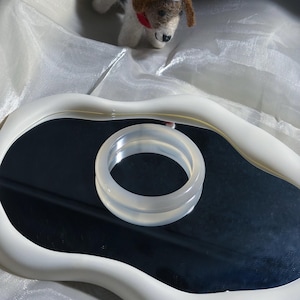May include: A smooth, translucent white bangle bracelet with a polished finish. The circular band features a clear, milky appearance and a rounded profile, reflecting light across its surface while resting on a dark, reflective surface.