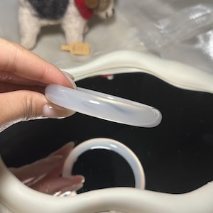 May include: A smooth, translucent white bangle bracelet with a polished finish. The circular band has a rounded profile and a consistent thickness throughout its circumference, appearing semi-opaque and light-reflecting under the bright lighting.
