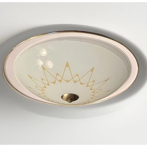 May include: A round flush mount ceiling light fixture featuring a white glass dome with a gold starburst pattern. The fixture has a metallic gold rim and a central gold finial cap that secures the glass shade to the ceiling mount base.