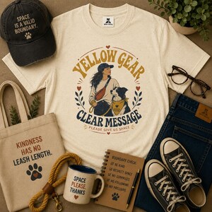 May include: A cream-colored t-shirt with a graphic of a person and a dog, a black baseball cap with the text SPACE IS A VALID BOUNDARY, a canvas tote bag with the text KINDNESS HAS NO LEASH LENGTH, a mug, a notebook, and black sneakers.