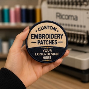 May include: A circular embroidered patch featuring a beige top section with the dark blue text CUSTOM EMBROIDERY PATCHES and a dark blue bottom section with the beige text YOUR LOGO/DESIGN HERE, separated by a horizontal line with small diamonds.