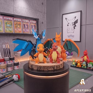 Puede incluir: Una colección de figuras de plástico de personajes Pokémon que incluye un gran Mega Charizard azul y negro, un Charizard naranja y dos figuras más pequeñas de Charmander naranja, sobre una base circular de madera con borde de corteza.