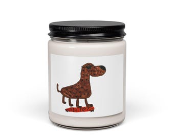 May include: A clear glass candle jar with a black lid featuring a white label. The label displays a brown dog wearing black sunglasses, standing on a red skateboard with black wheels. The candle wax inside the jar is a light cream color.