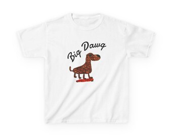 May include: A white short-sleeve t-shirt featuring a brown dog graphic with a textured pattern standing on a red skateboard. Above the dog, the text Big Dawg is printed in a black cursive font. The design is centered on the front of the shirt.